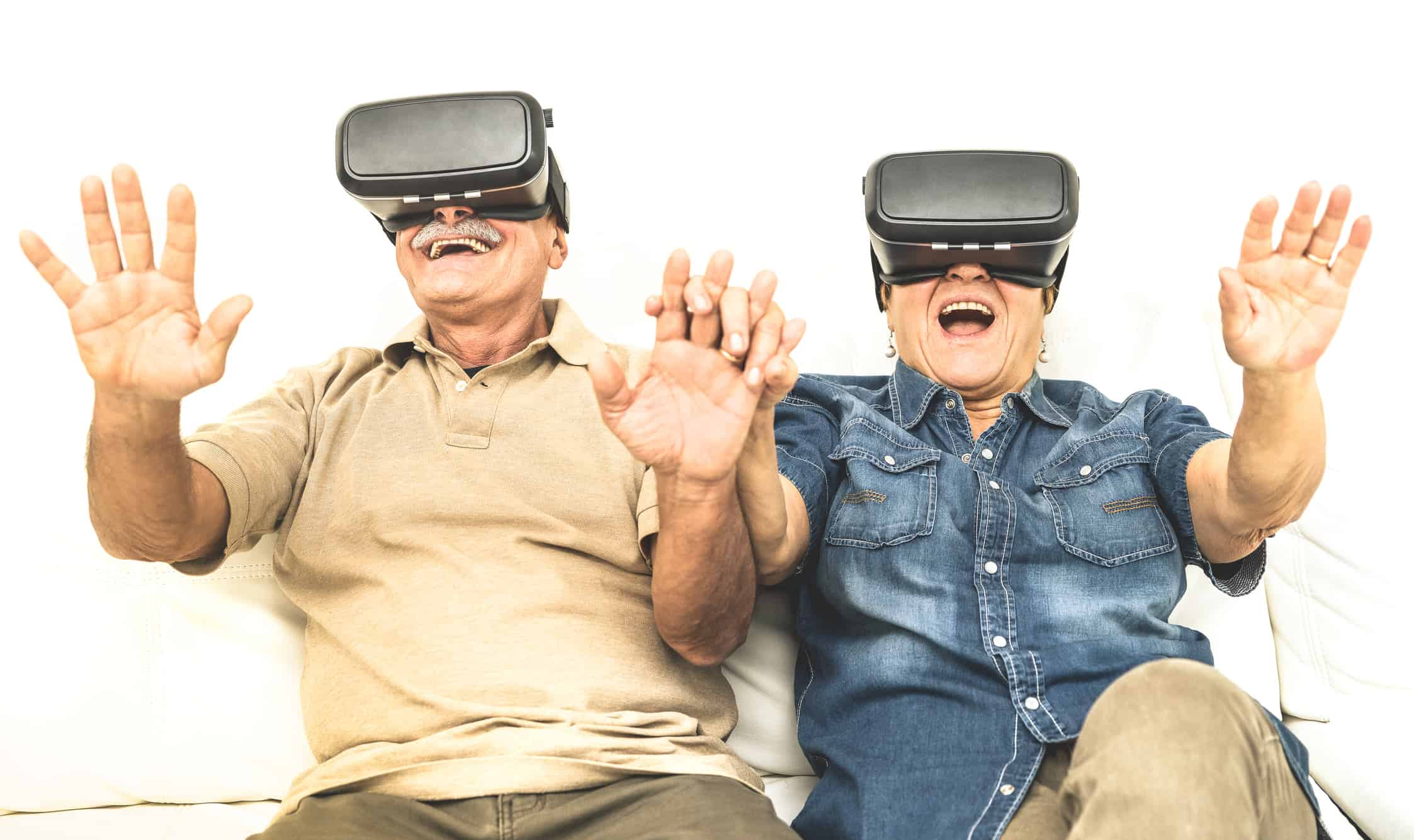 Senior mature couple having fun together with virtual reality headset sitting on sofa – Happy retired people using modern vr goggle glasses – New trends and technology concept and funny active elderly